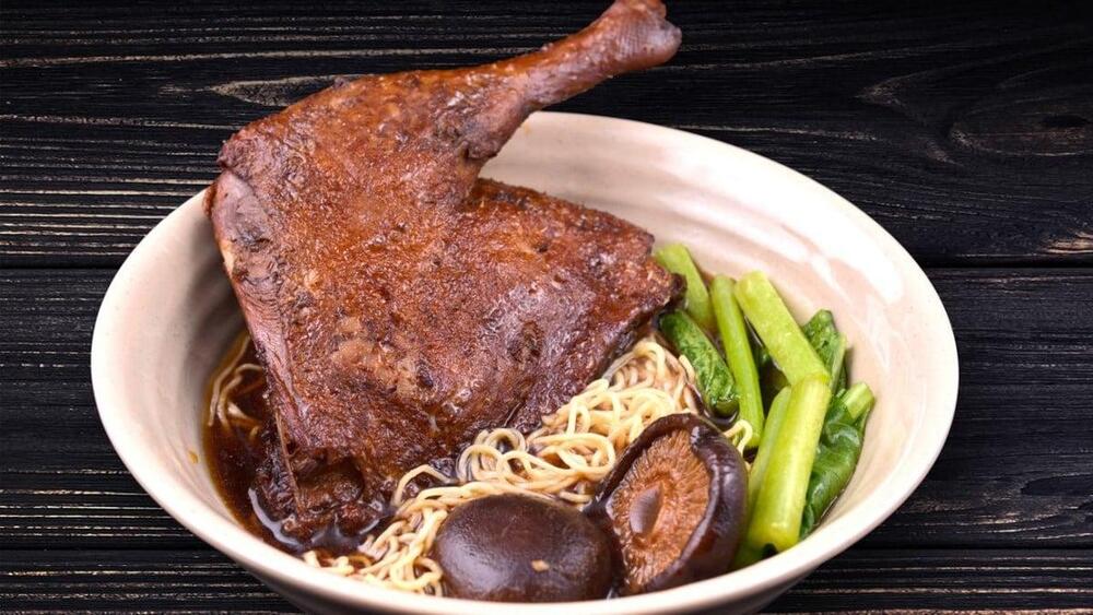A comforting, hearty dish where tender roasted duck is served in a flavorful broth with noodles, garnished with herbs and fried shallots