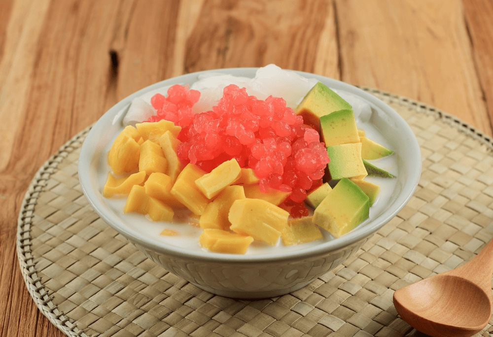 A rainbow bowl of hoa qua dam featuring colorful fruit pieces - pink dragon fruit, red watermelon, yellow mango, white longan, with crushed ice (Source: Canva)