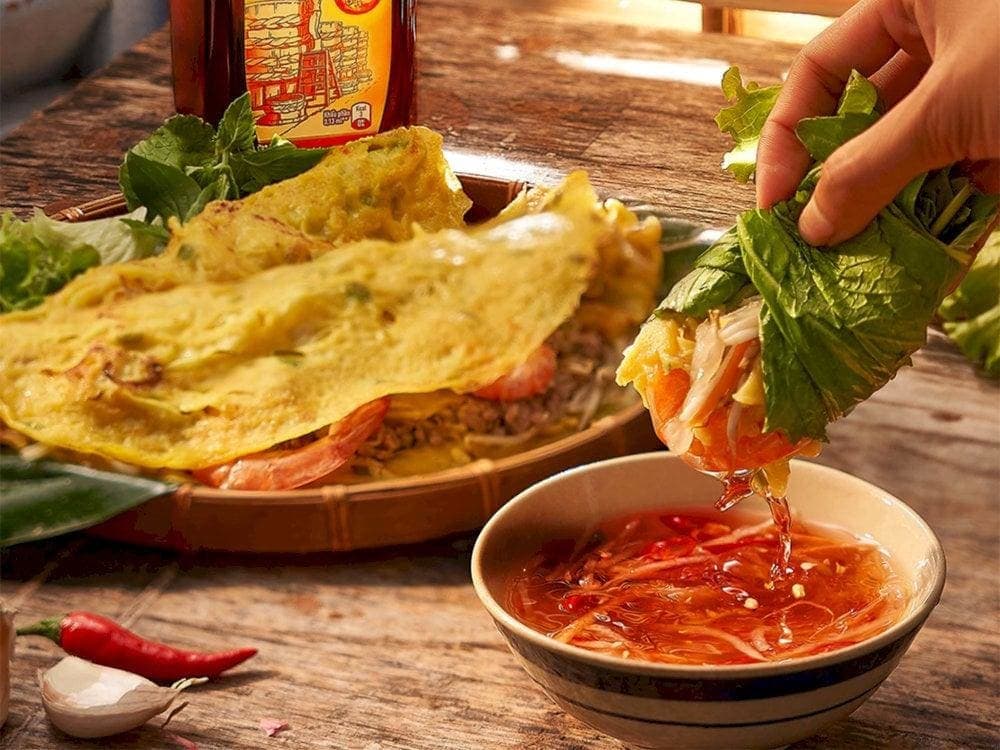 Banh xeo is typically served with fresh herbs, lettuce, and rice paper for wrapping, then dipped in sweet and tangy fish sauce