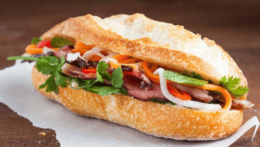 Golden crispy banh mi sandwich filled with colorful pickled vegetables and fresh cilantro