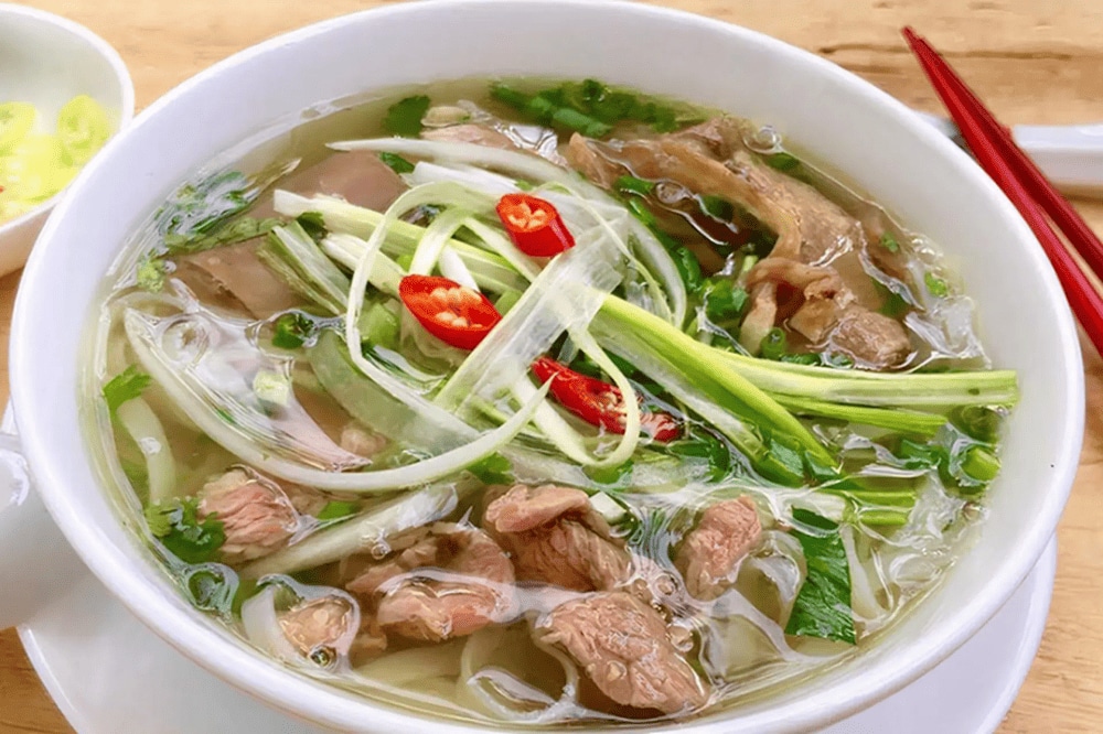 Steaming bowl of pho bo with fresh herbs and lime wedges on the side