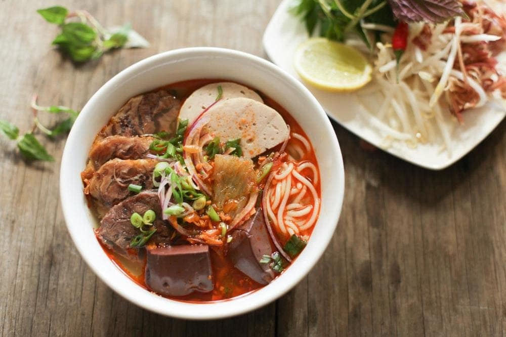 Vibrant red spicy noodle soup with thick rice noodles and herb garnishes