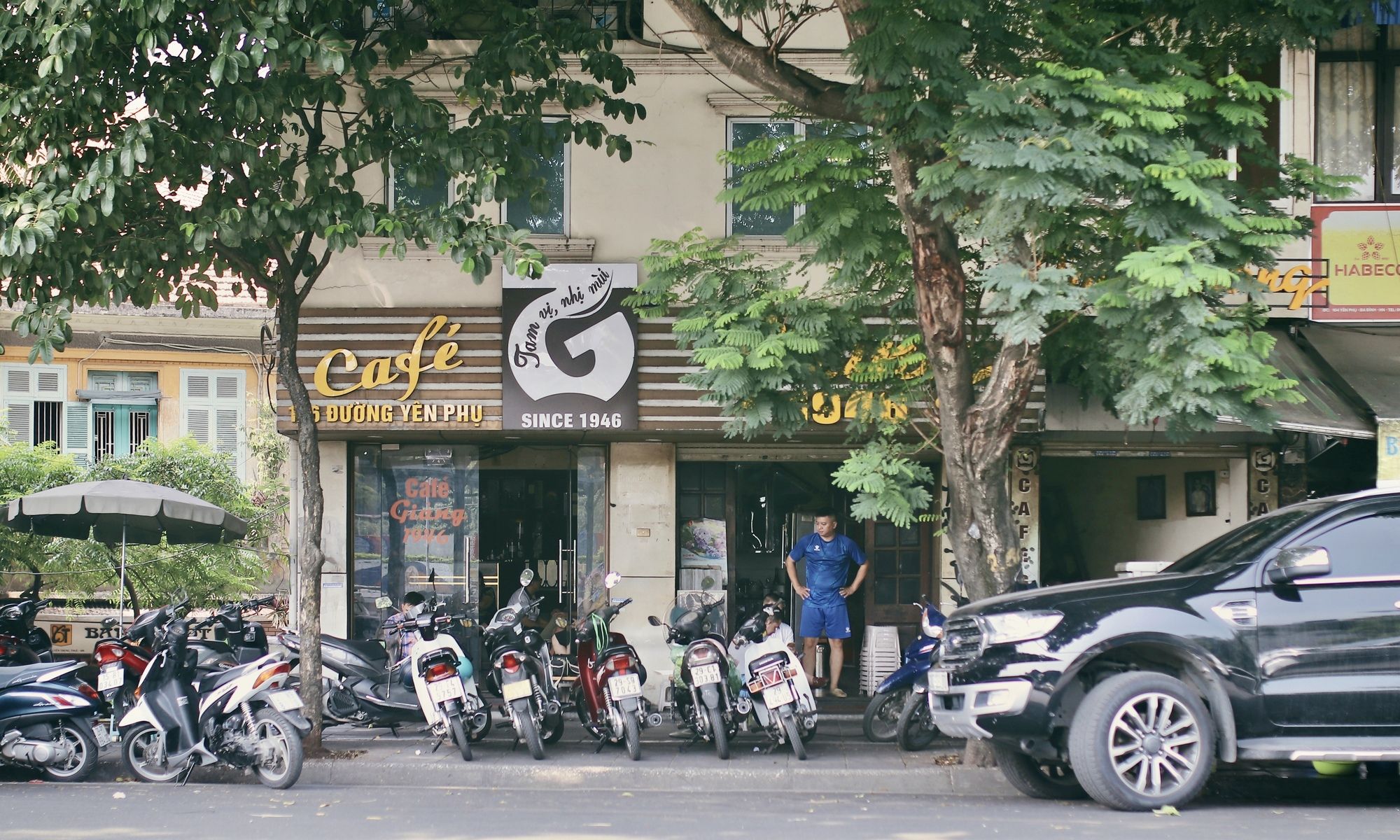 Bustling street scene showing traditional Vietnamese coffee vendor with customers sitting on tiny plastic stools